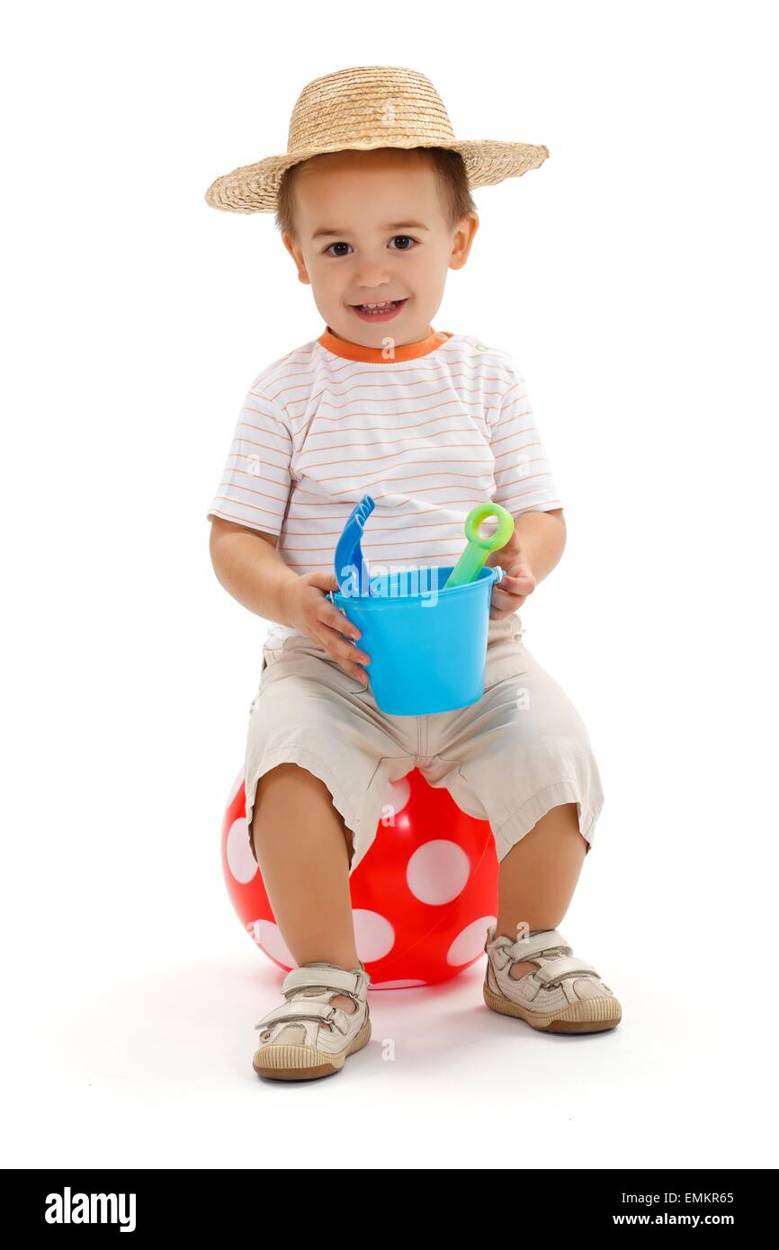 Smiling little boy sitting on big, red dotted ball, holding sandbox toys Stock Photo