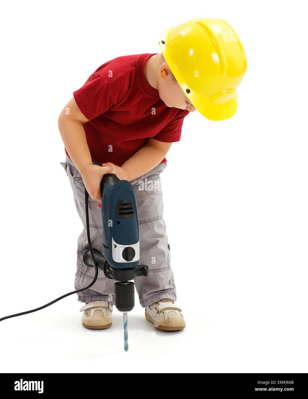 Little boy drilling in ground with real drill, wearing yellow protective helmet, imitating handyman Stock Photo