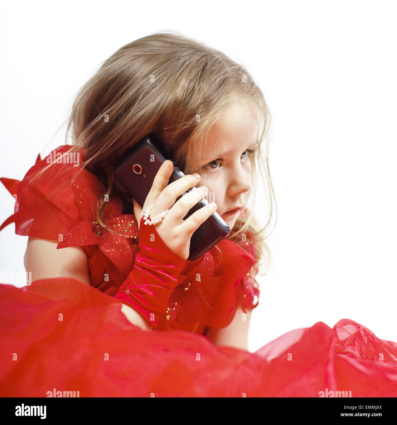 Cute little girl dressed in ball gown playing with smartphone and smiling, isolated on white background Stock Photo