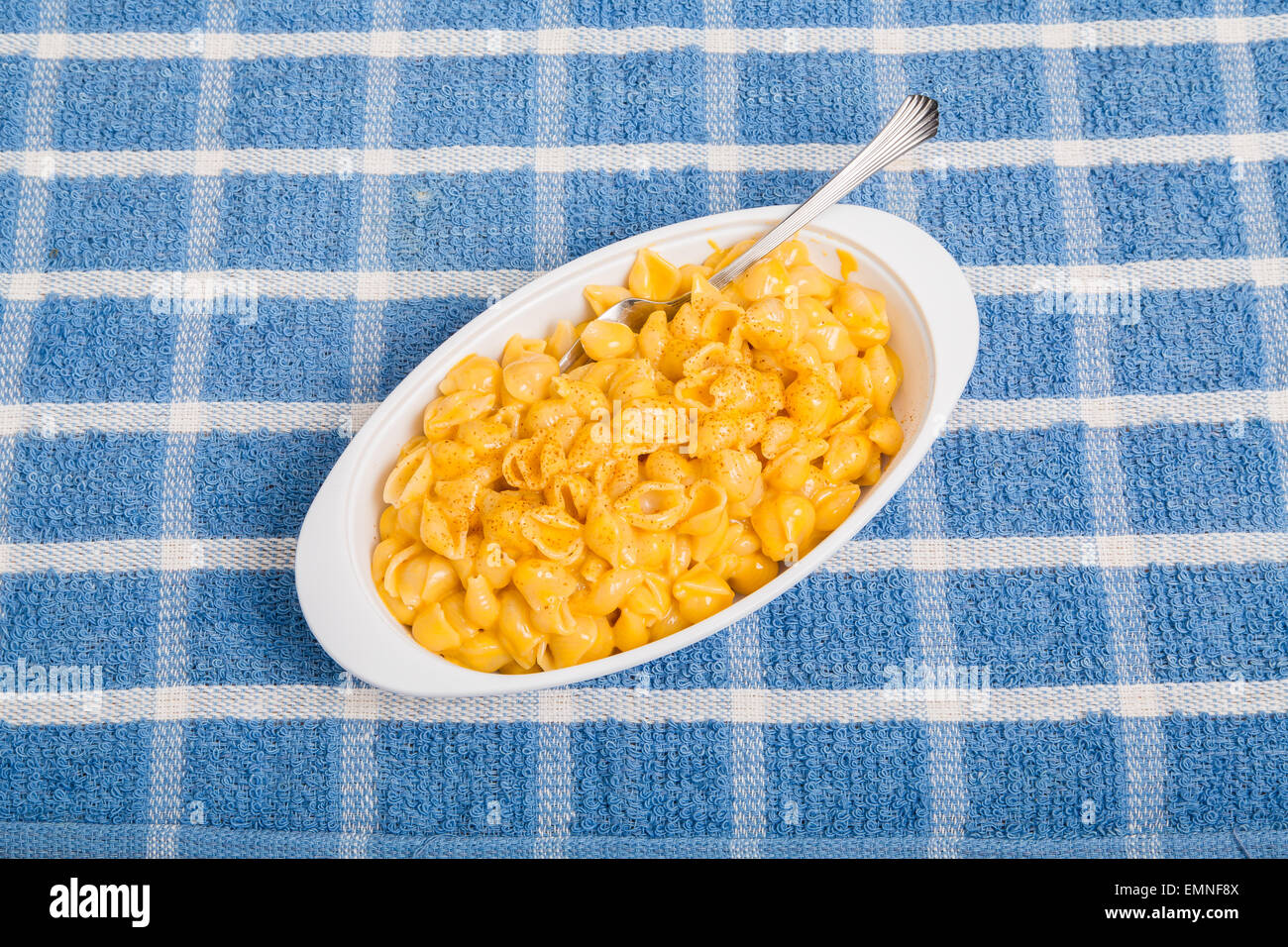 A white dish of macaroni and cheese with fork on blue plaid towel Stock Photo