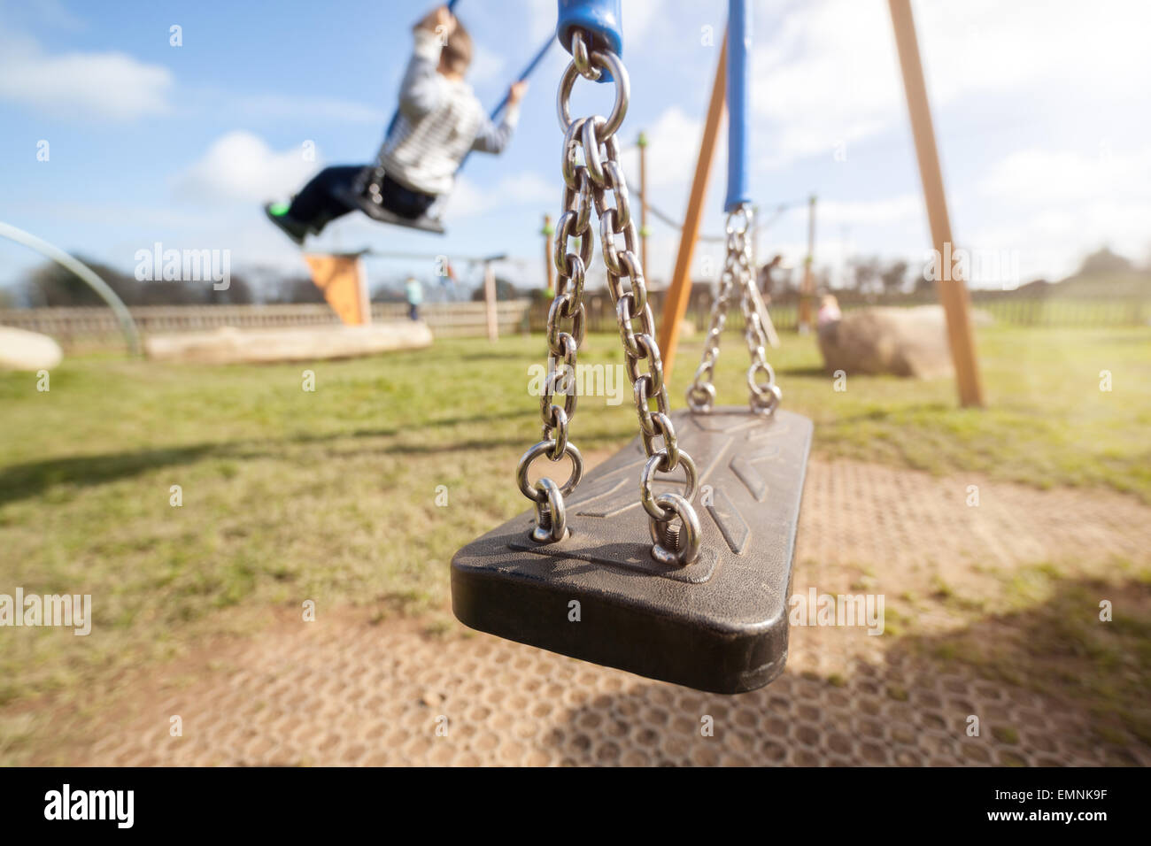 Empty playground swing with children playing in the background concept for child protection, abduction or loneliness Stock Photo