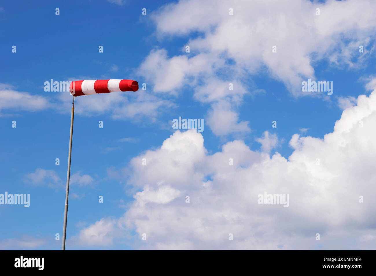 Image of a red white wind vane against blue sky with white clouds Stock Photo