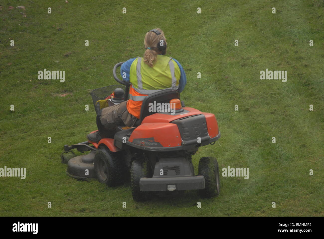 Man cutting grass with ride-on lawn mover. Gardener maintaining open space. Maintenance of parkland. Stock Photo