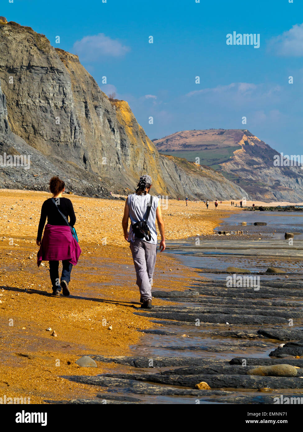 Couple walking on beach at Charmouth on the Jurassic Coast in West Dorset England UK with Golden Cap cliffs in the distance Stock Photo
