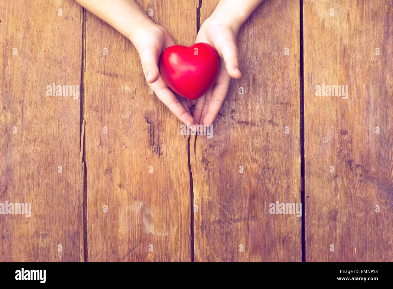 red heart in hands over vintage wooden background Stock Photo