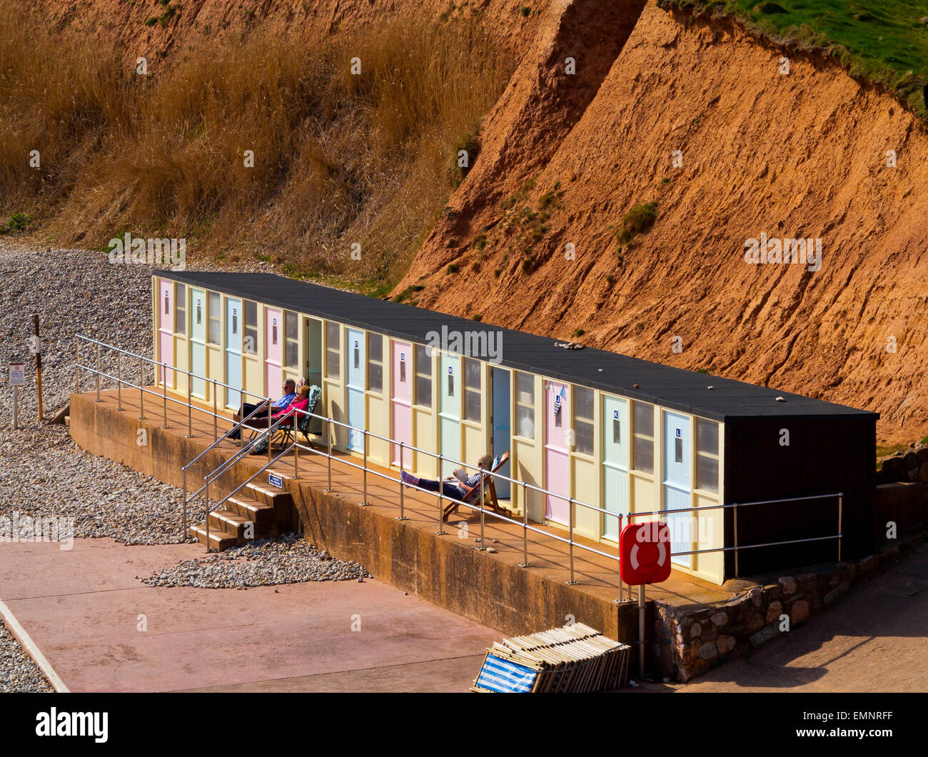 Tourists relaxing outside beach shelter below the cliffs at Sidmouth a seaside resort in South