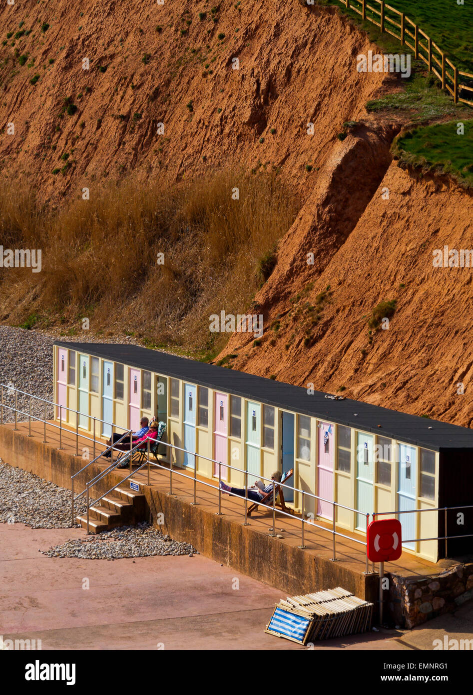 Tourists relaxing outside beach shelter below the cliffs at Sidmouth a seaside resort in South