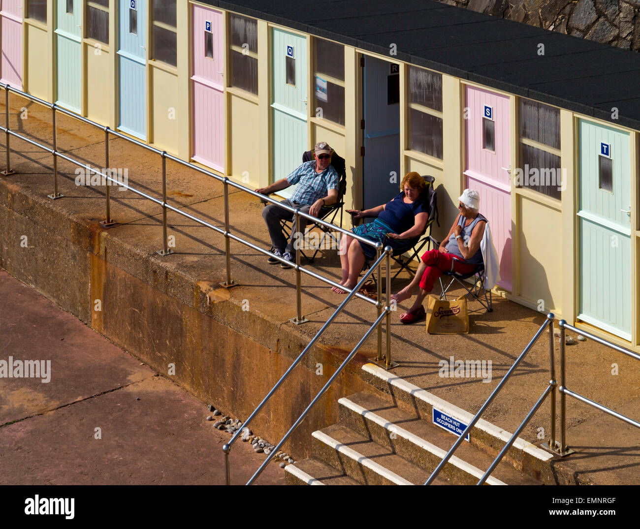 Tourists relaxing outside beach shelter below the cliffs at Sidmouth a seaside resort in South Devon England UK Stock Photo