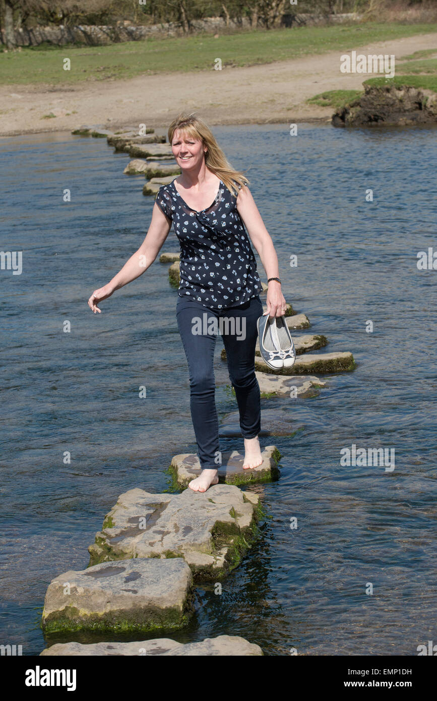 Stepping stones on the Ogmore River in South Wales and a woman is seen crossing Stock Photo