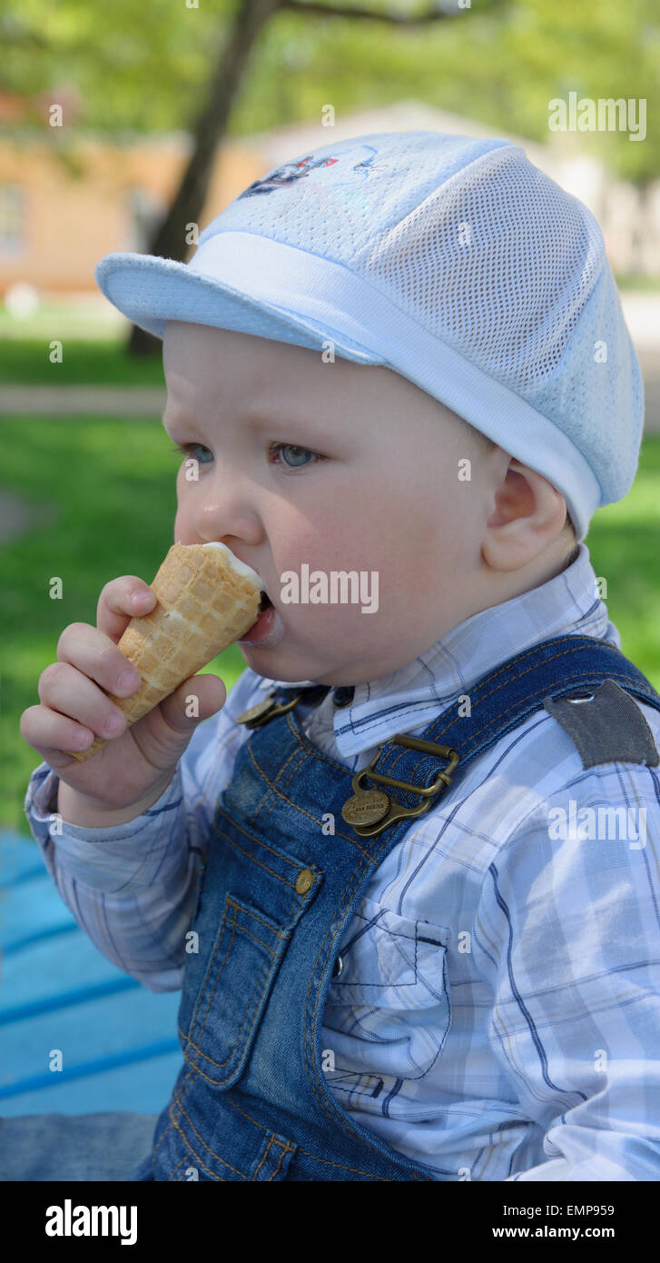 The boy in a jeans suit sits on a shop and eats ice cream Stock Photo