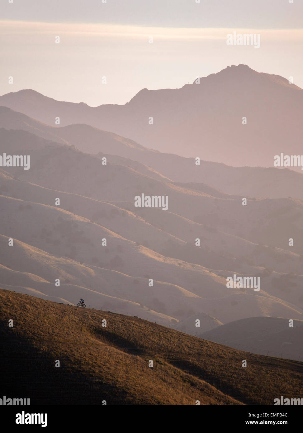 Mountain biker riding a ridge in the Wither Hills with the Blairich Range beyond. Marlborough, New Zealand. Stock Photo