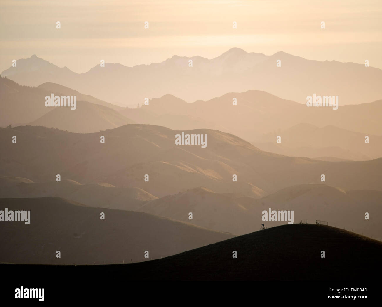 Mountain biker riding a ridge in the Wither Hills with the Blairich Range beyond. Marlborough, New Zealand. Stock Photo