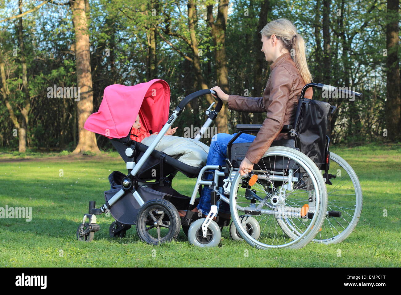 A Mother in wheelchair pushing a pram with baby Stock Photo