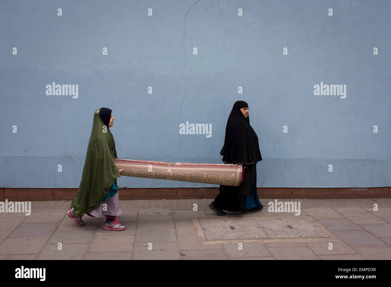Muslim women carry heavy carpet along street on Walworth Road, Elephant & Castle, London borough