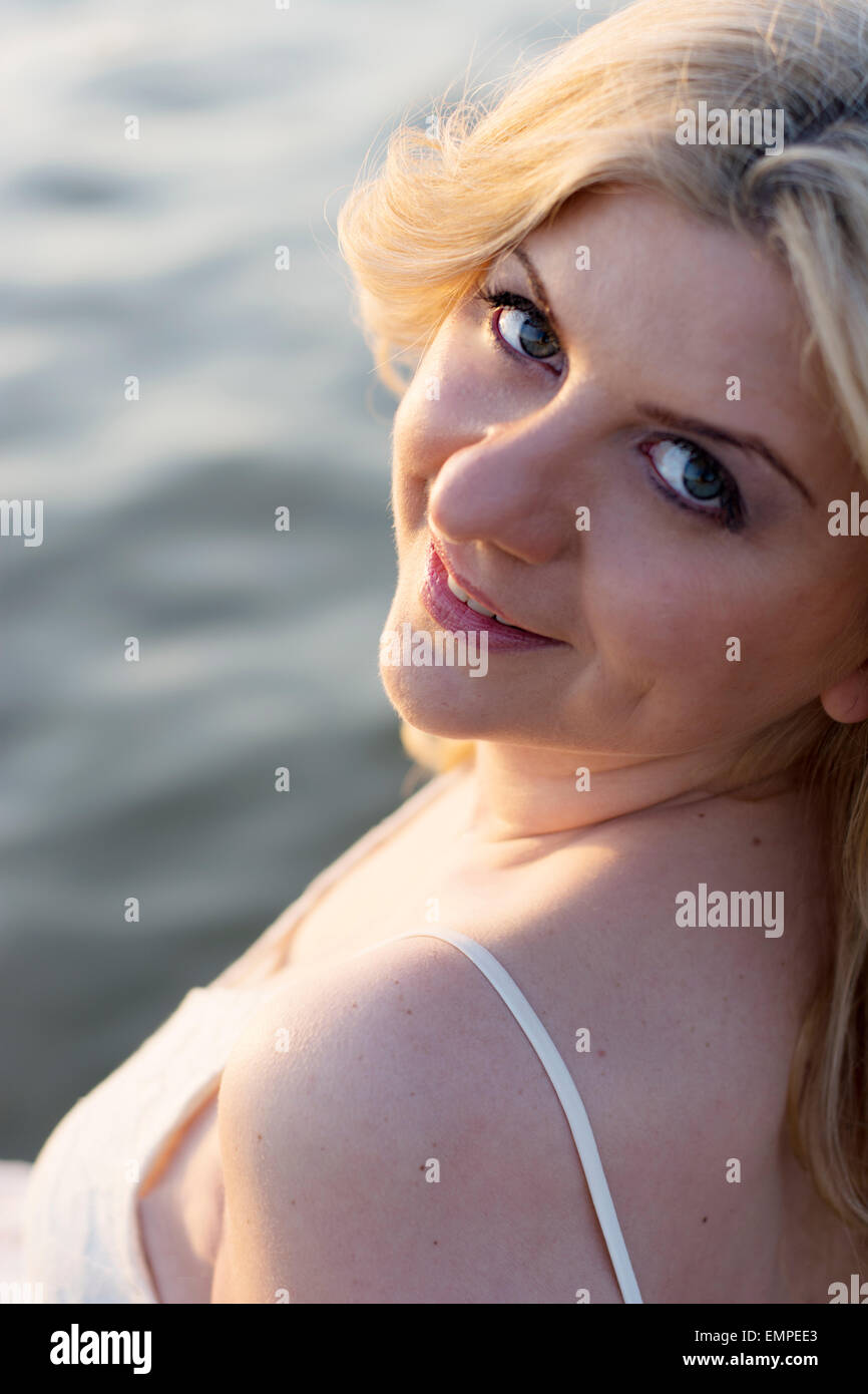 Portrait of a blond woman with lake behind her enjoying sun. Stock Photo