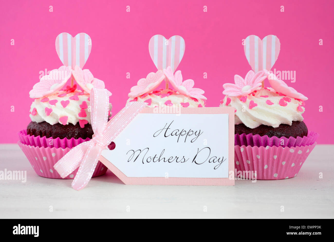 Happy Mothers Day pink and white cupcakes with heart shape topper and hearts and flowers decorations on vintage white wood table Stock Photo