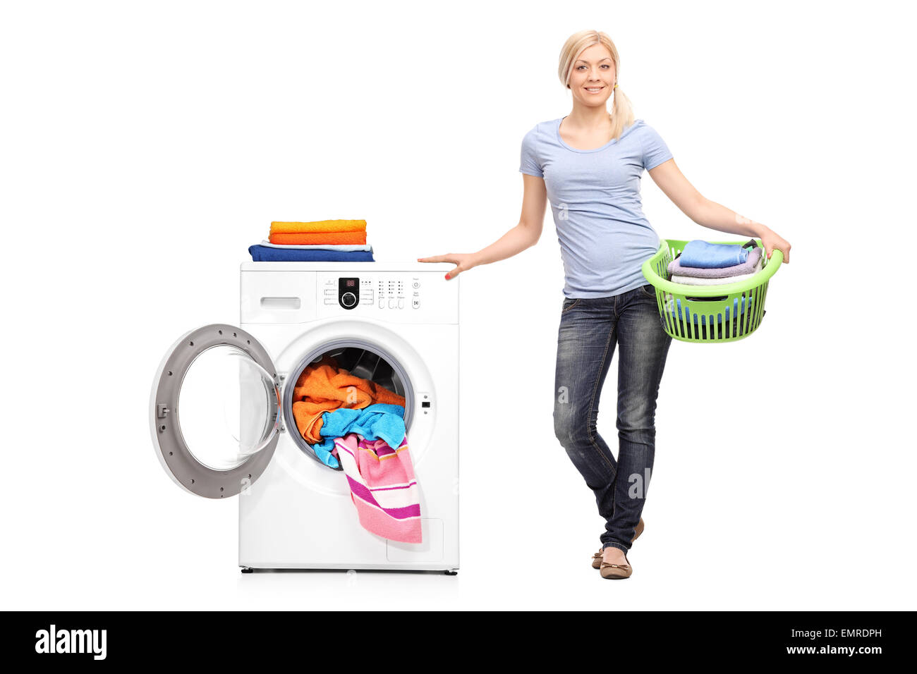 Full length portrait of a young woman holding a laundry basket full of folded clothes and posing next to a washing machine Stock Photo