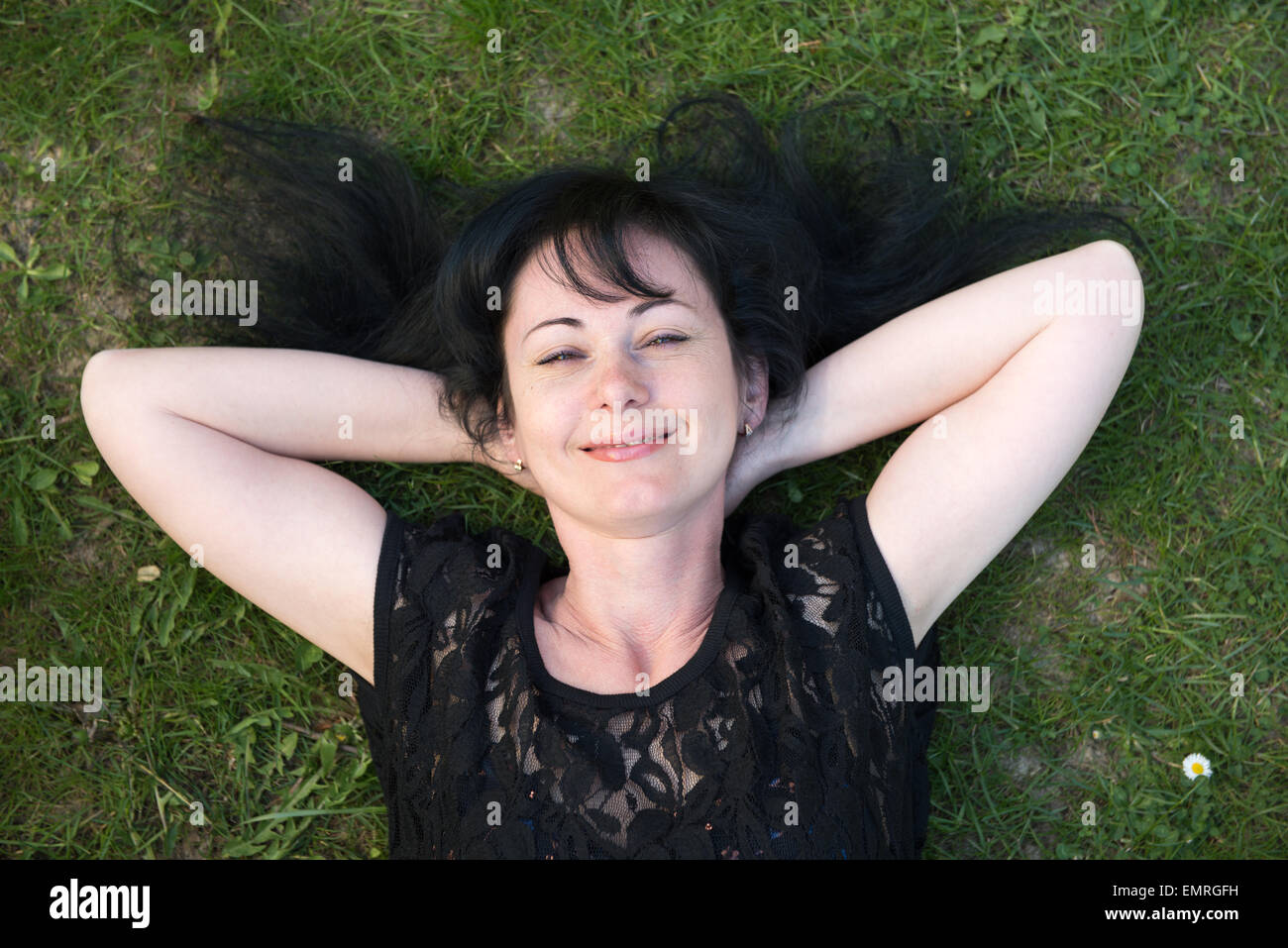 woman with black dress and black hair lying on the grass and smiling Stock Photo