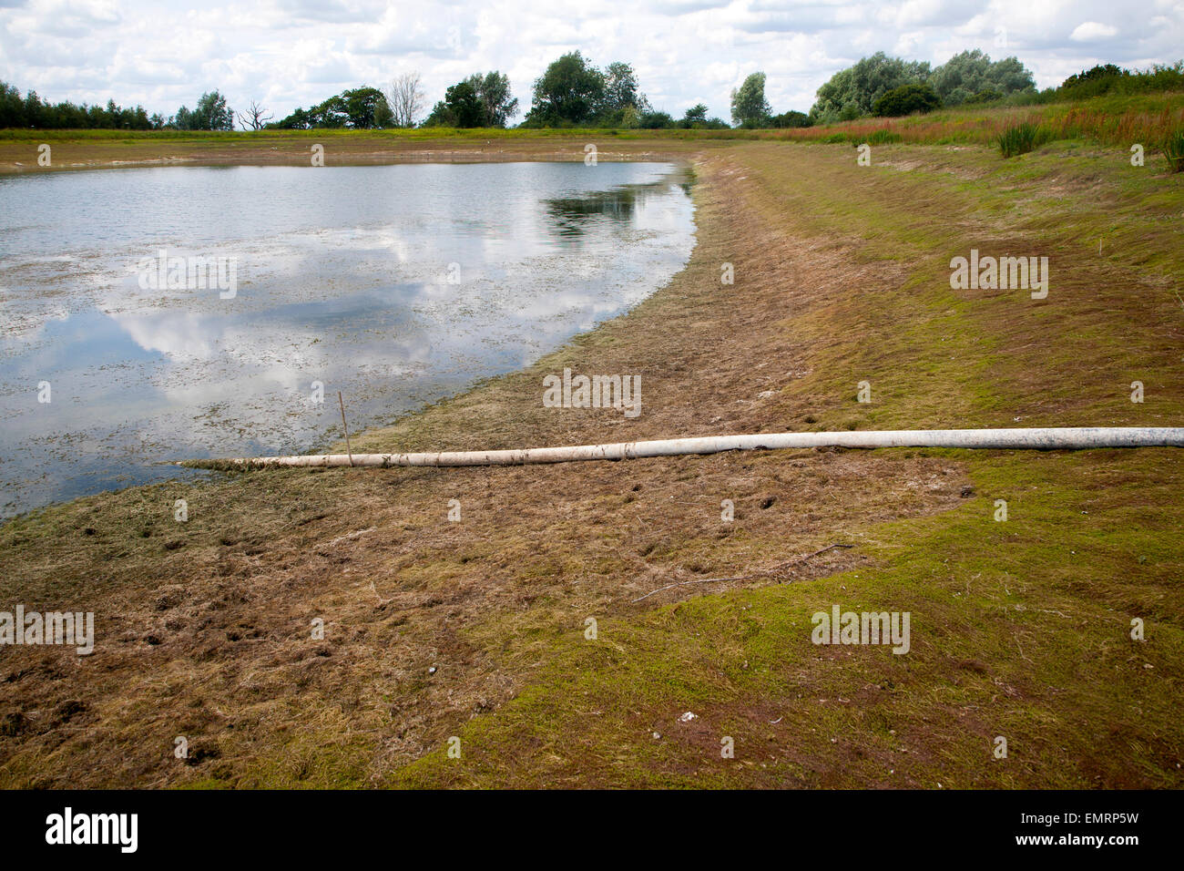 Irrigation pipe water reservoir lake at low level in summer Sutton, Suffolk, England Stock Photo