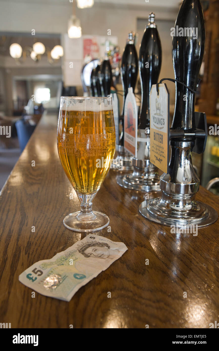 A pint of lager and a £5 note on a bar in a pub. Stock Photo