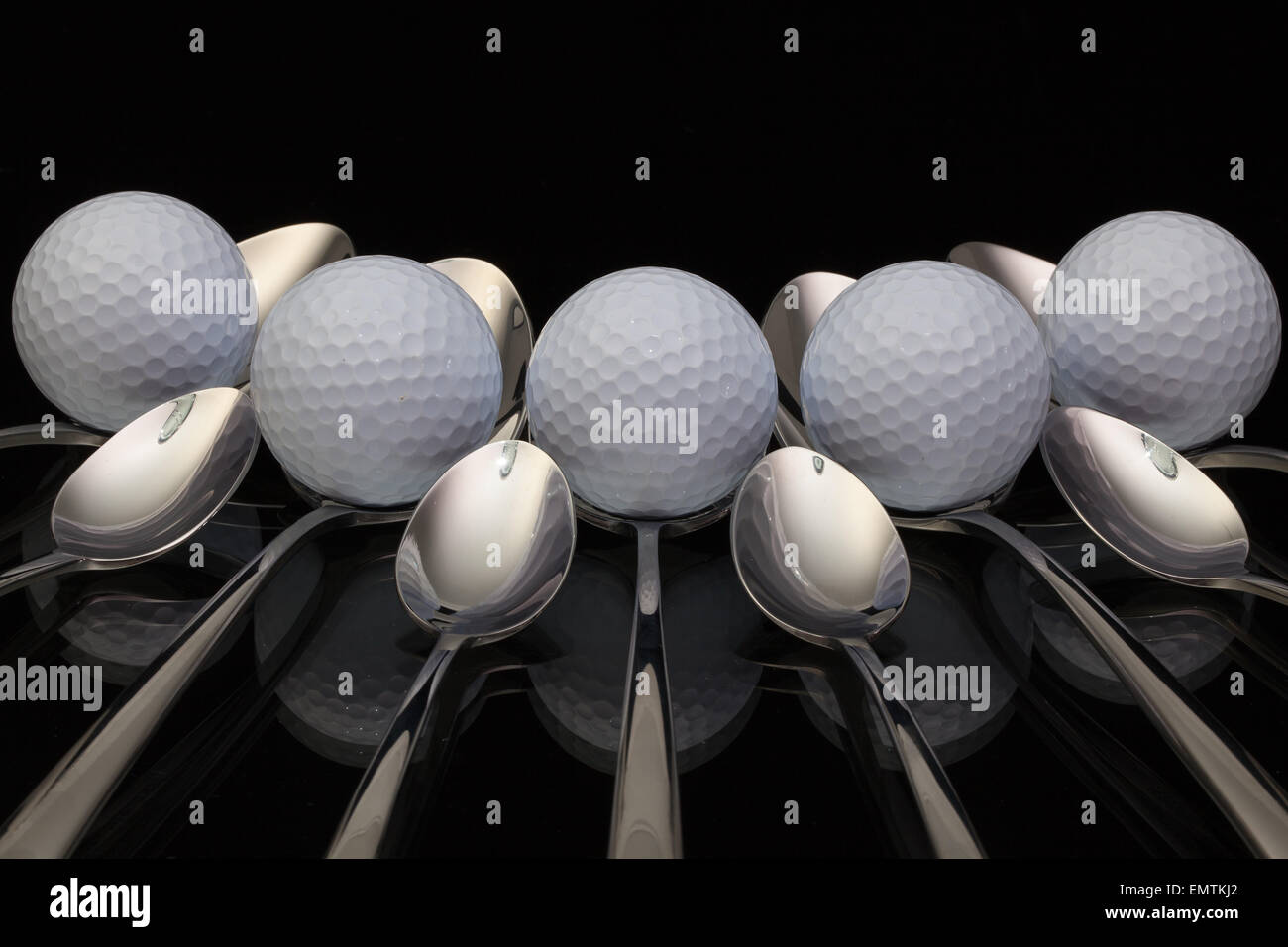 Golf Balls And Nine Spoons On A Black Glass Desk Stock Photo