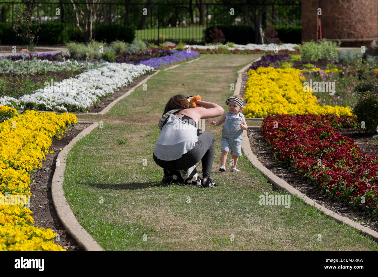 A young, dark-haired Caucasian mother photographs her one year old baby girl in a public park. Oklahoma City, Oklahoma, USA Stock Photo