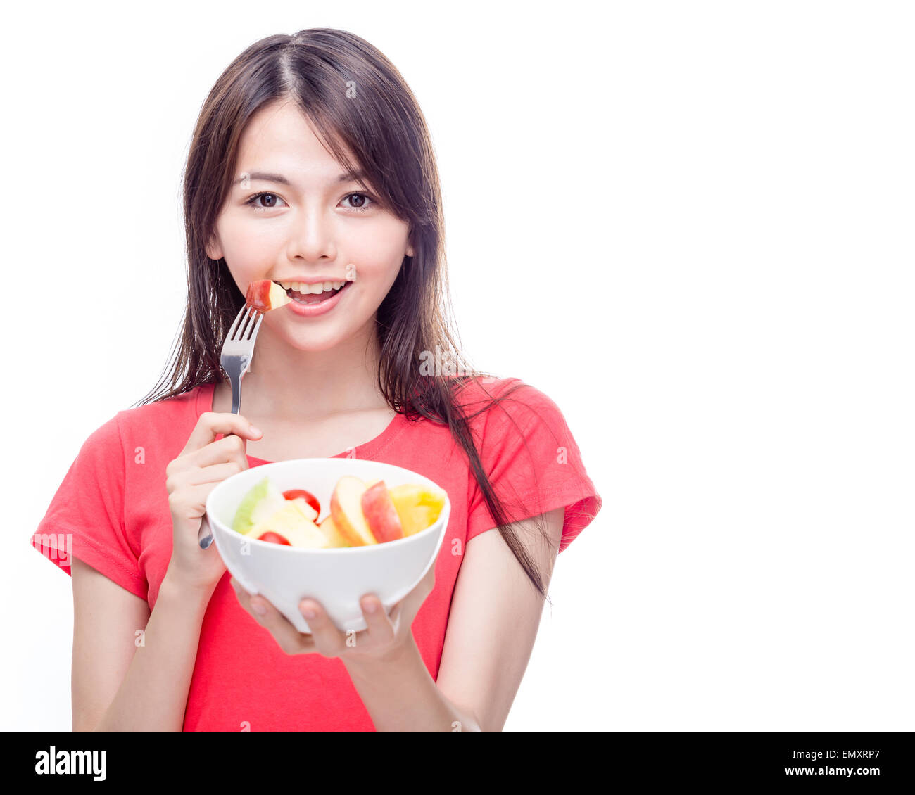 Young Chinese woman holding bowl of fruit, eating apple off fork Stock