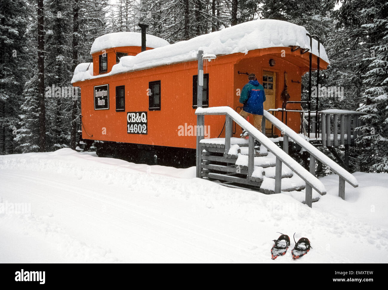 A snowshoeing guest enters his lodging that is a restored 1895 railroad caboose, one of eight historic caboose railcars that are major attractions at the Izzak Walton Inn at the edge of Glacier National Park in Montana, USA. The orange-painted car from the Chicago, Burlington and Quincy line now features a full-size bed, bathroom with shower, and well-equipped kitchenette. The remote inn is open year-round and reached by rail with Amtrak, America's major passenger rail service. Stock Photo