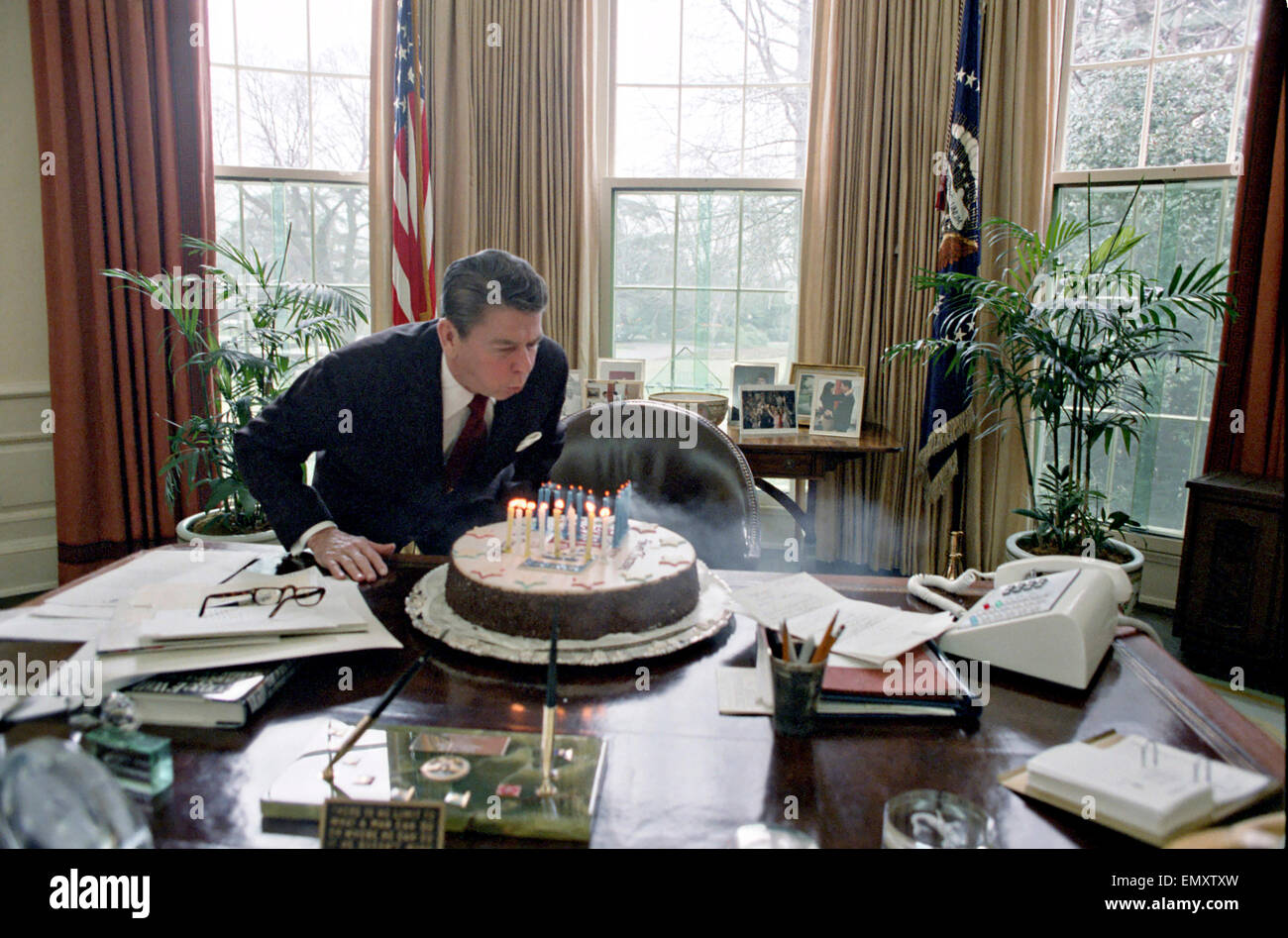 US President Ronald Reagan blows out candles on cake while celebrating his birthday party in the Oval Office of the White House February 5, 1982 in Washington, DC. Stock Photo