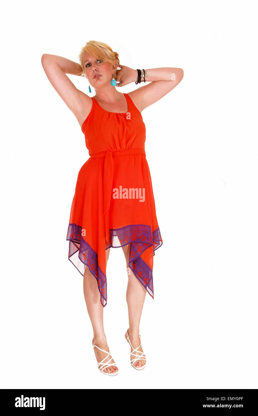 A pretty woman in a red dress standing with her hands behind her head ...
