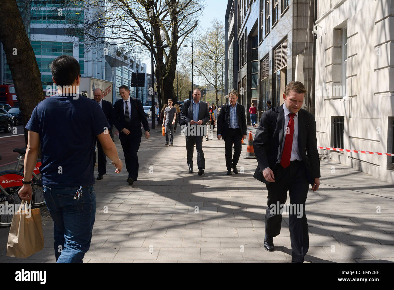 man in jeans & T-shirt walking past men in suits on pavement in London Stock Photo