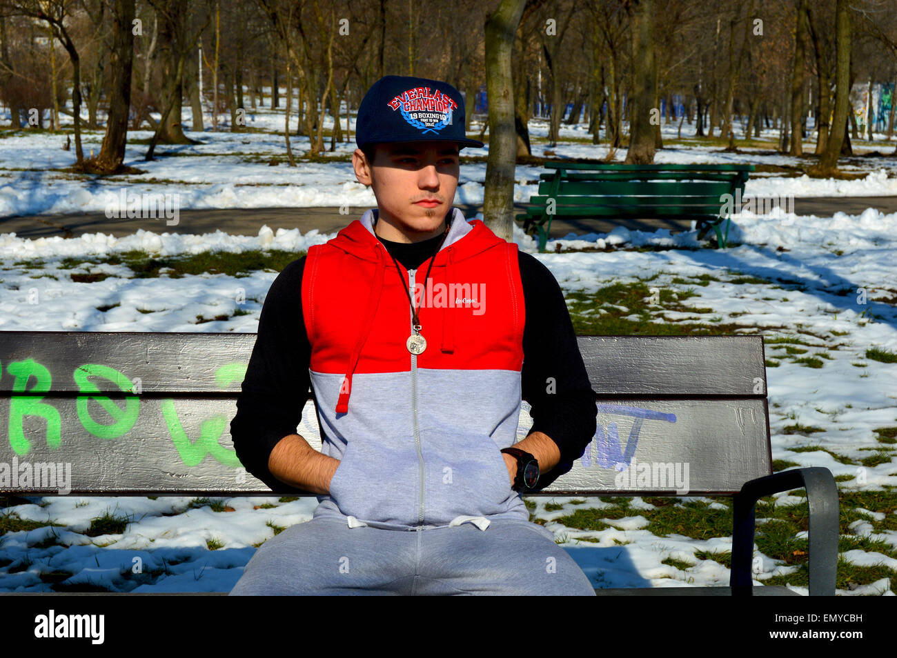 Man wearing hoodie, cap and necklace sitting on park bench Stock Photo