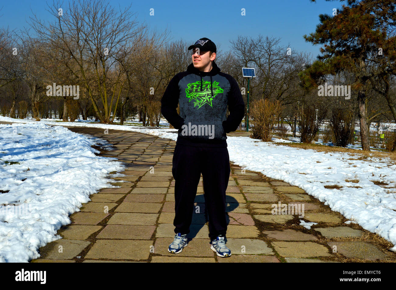 Man with hoodie and cap walking through park Stock Photo