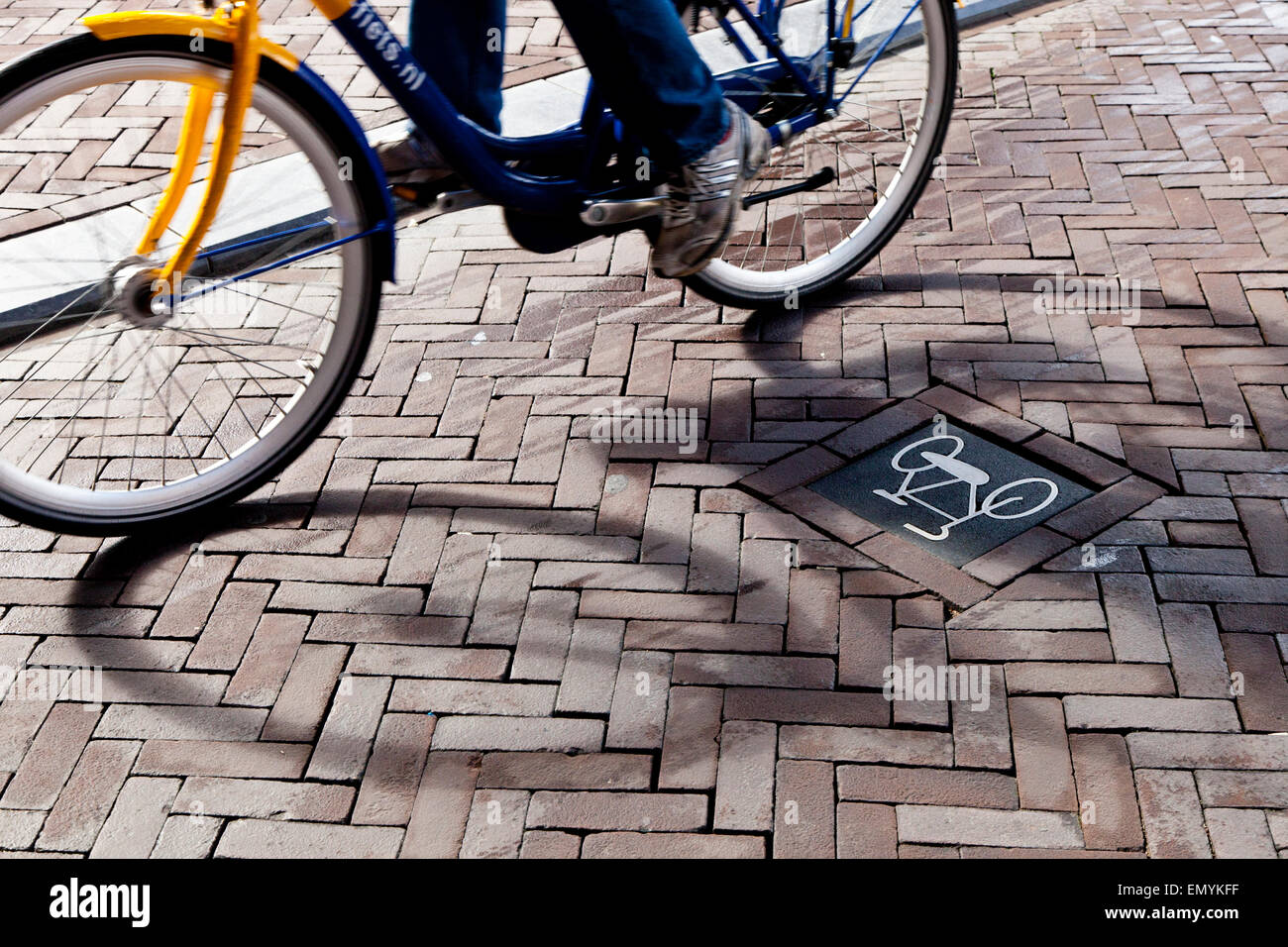 A bike sign on the road with the shadow of a cyclist going by Stock Photo