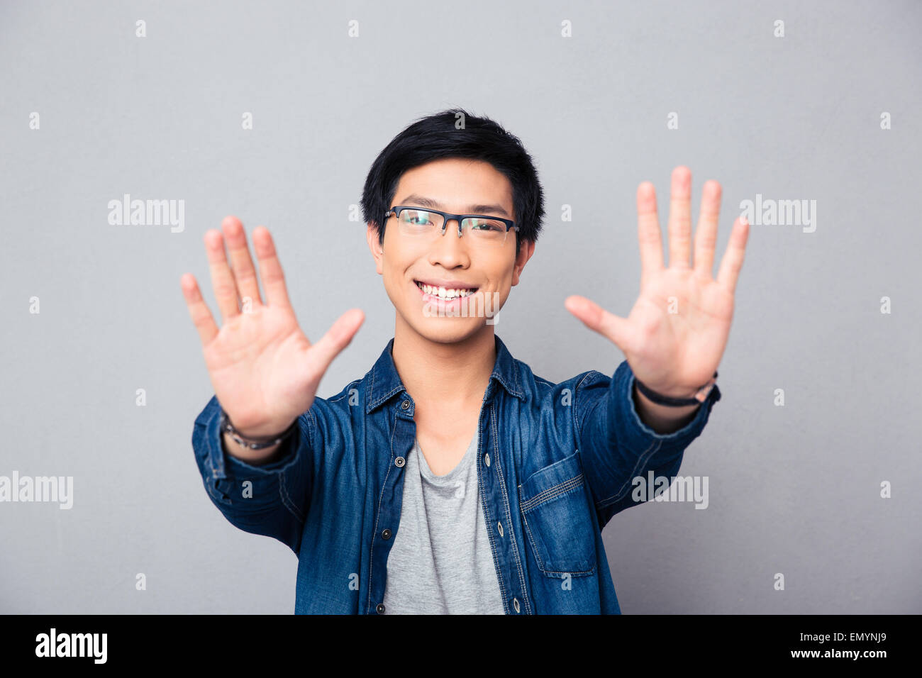 Happy asian man in glasses making stop gesture with palm over gray background Stock Photo