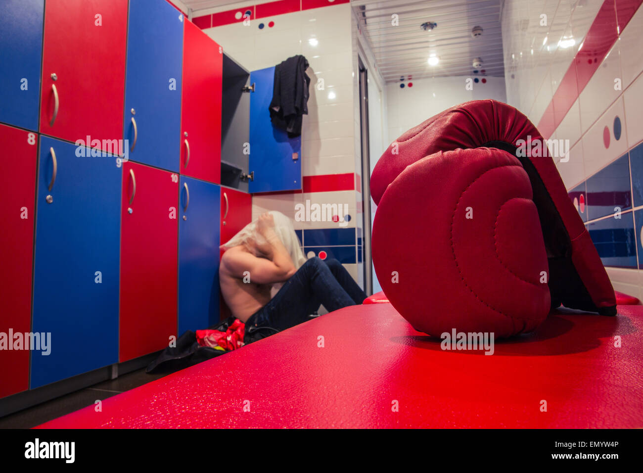 Tired man sitting on the floor in the locker room after finishing training Stock Photo