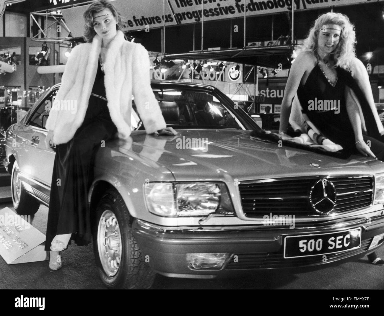 Two models draped over the bonnet of the new Mercedes 500 Sec at the 1982 Motor Show. 19th October 1982 Stock Photo