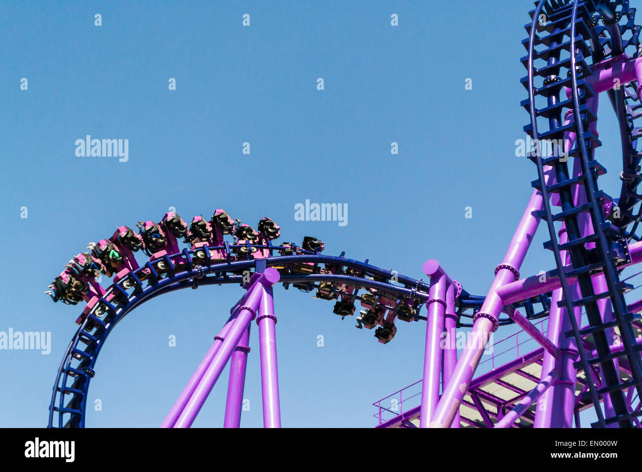People riding a purple rollercoaster against a blue sky Stock Photo