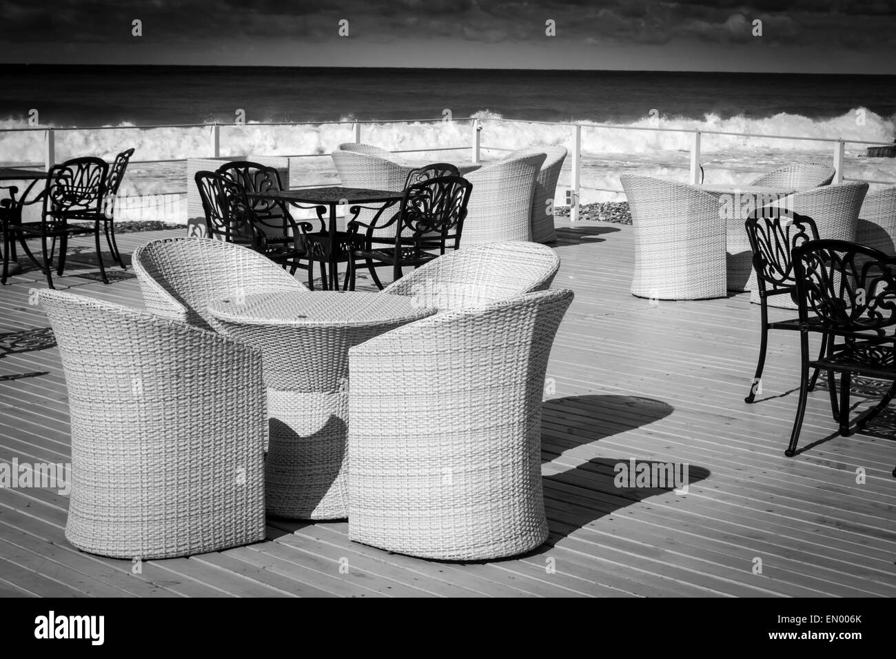 Empty wicker and black iron chairs wait for tourists in the cloudy sun cast sky Stock Photo