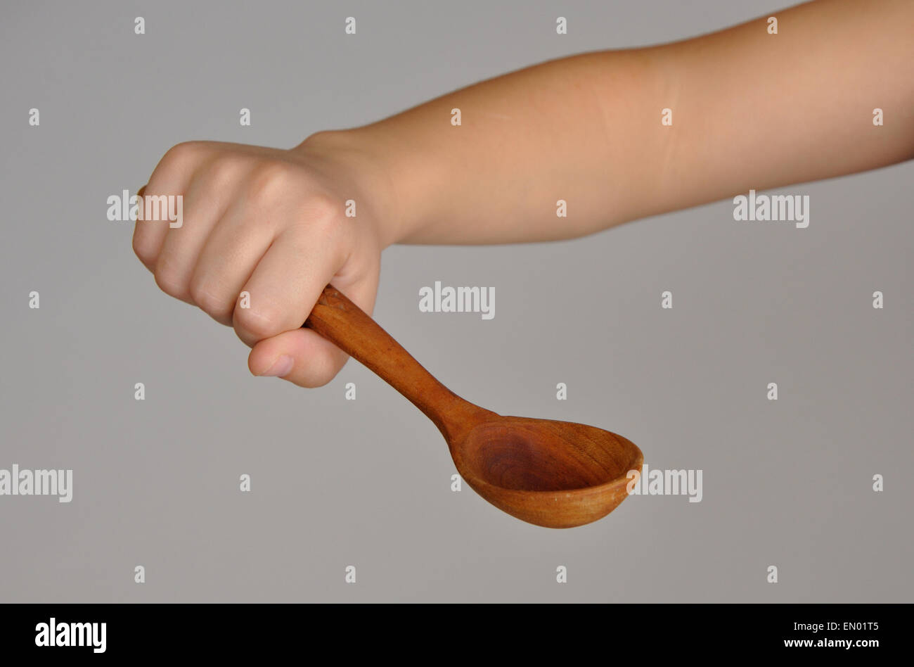 Wooden spoon in baby hand over gray background Stock Photo