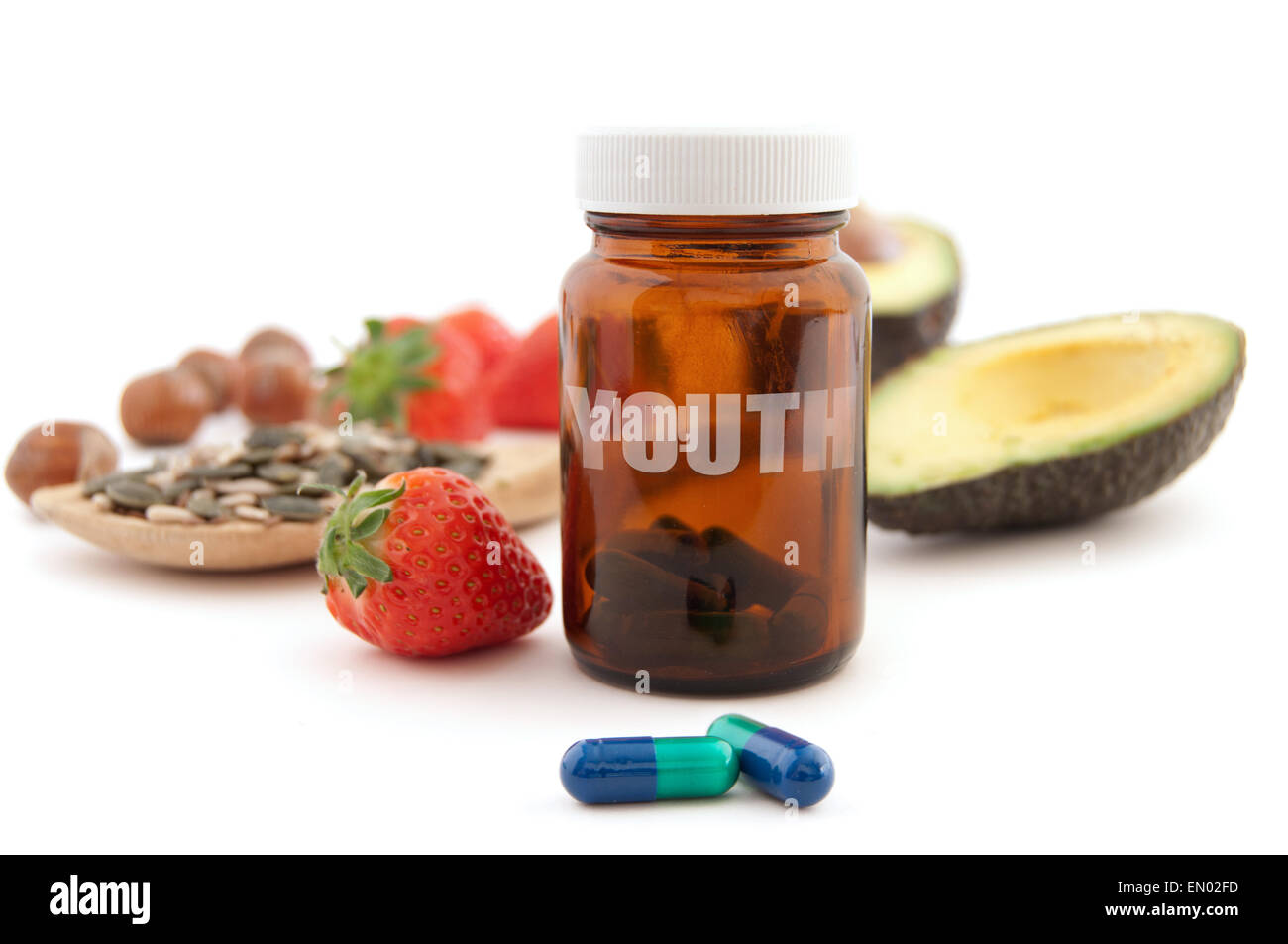 Anti-aging pills surrounded by nutritious superfoods including avocado, pumpkin seeds and berries Stock Photo