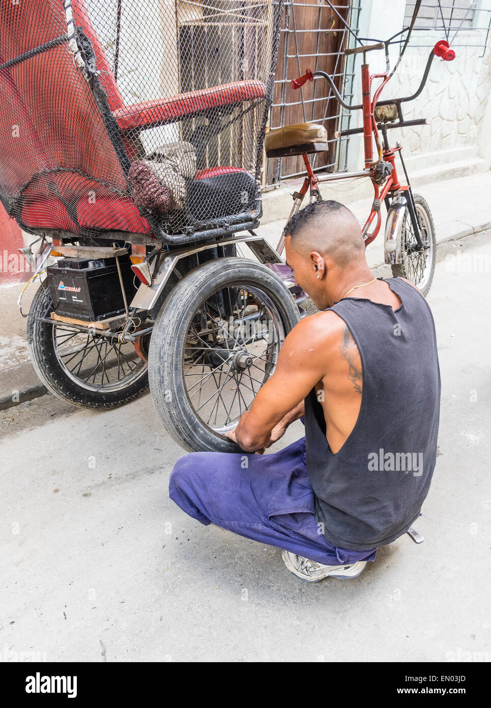 A male Hispanic Cuban pedicab driver changes a flat tire on his 3