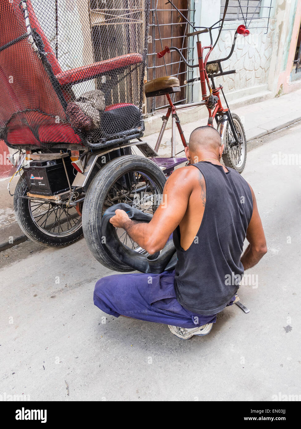 A male Hispanic Cuban pedicab driver changes a flat tire on his 3