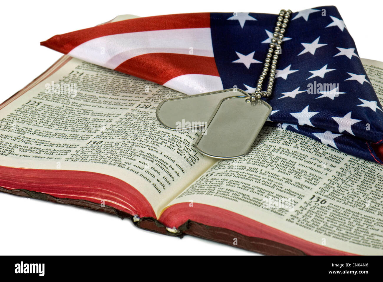 Military dog tags on open Bible with folded American flag isolated on white. Stock Photo