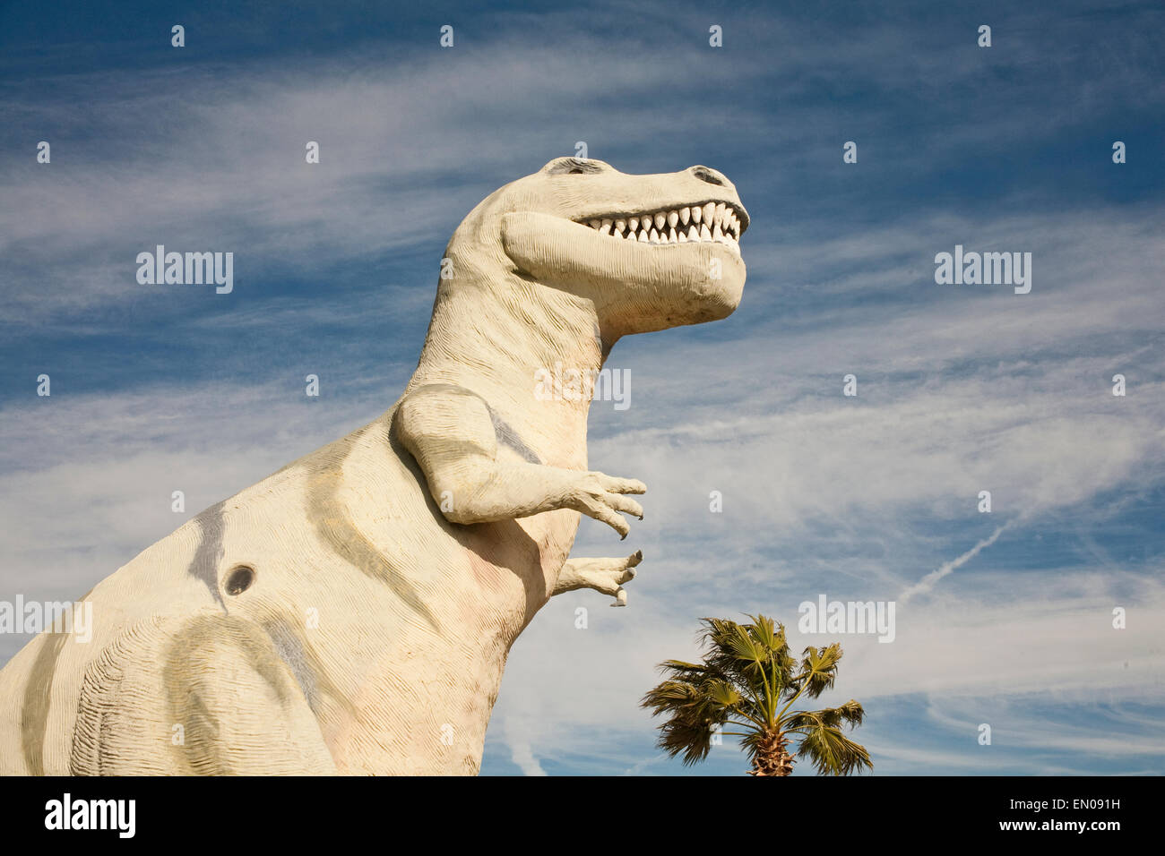 A tyrannosaurus rex statue sits in the bright sun against a blue sky in the California desert. Stock Photo