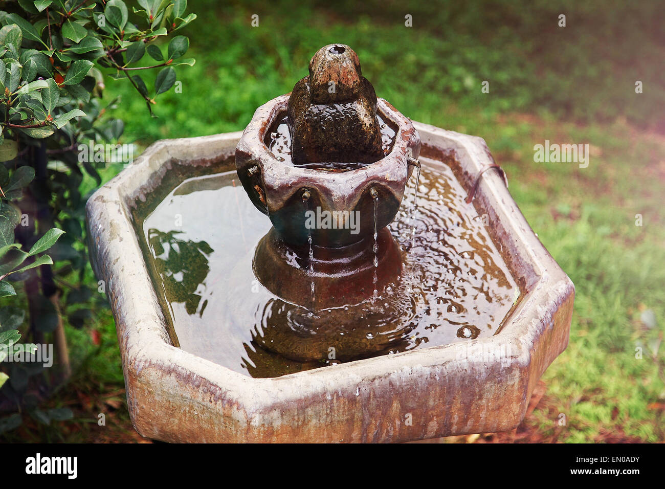 Water flows down a colorful fountain in a lush green yard reflecting an overcast sky. Stock Photo