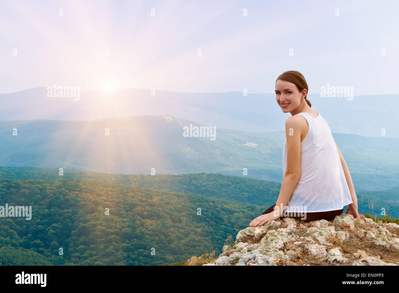 Happy smiling girl sitting on a cliff side. Woman relaxing in mo Stock Photo