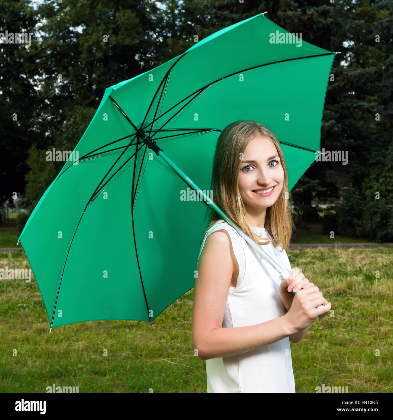 Beautiful smiling girl holding a green umbrella in a park Stock Photo