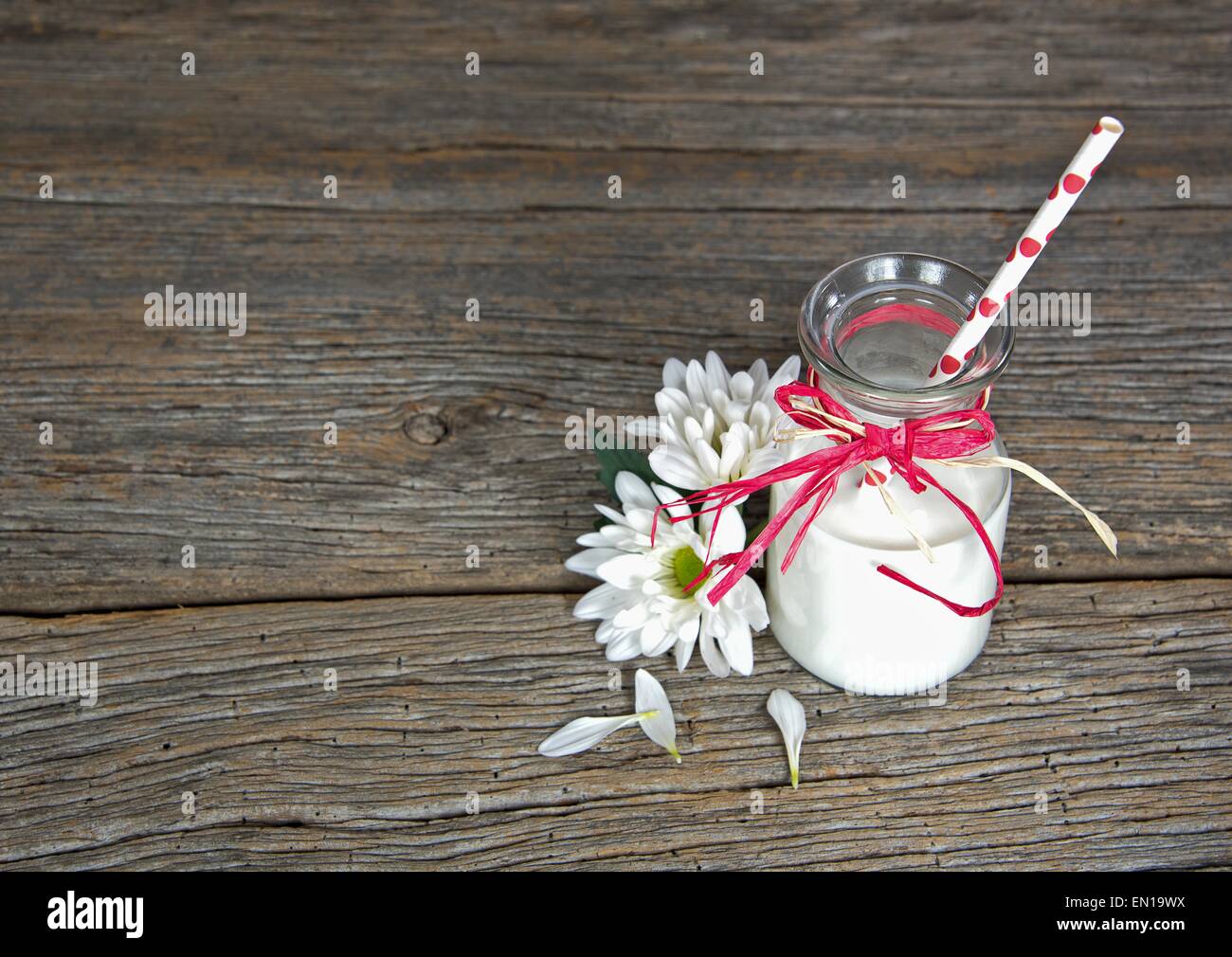 White milk in a retro glass bottle with polka dot straw and daisies on rustic wood. Stock Photo