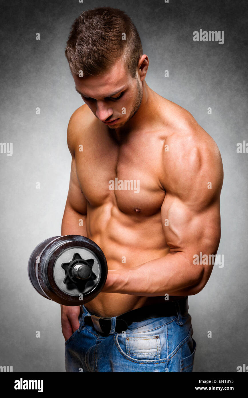 Young man with well trained body, biceps, abs and pecs holds a dumbbell Stock Photo